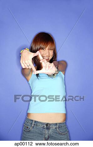 Stock Image - Young woman against blue background, making hand sign. Fotosearch