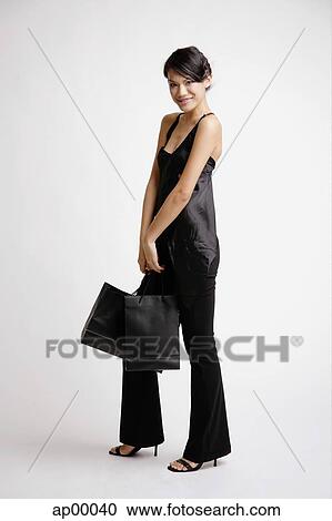 Stock Image - Young woman carrying shopping bags, smiling at camera. Fotosearch