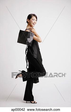 Young woman carrying shopping bags, standing on one leg, side view View Large Photo Image Stock Image - Young woman carrying shopping bags, standing on one leg, side view. Fotosearch