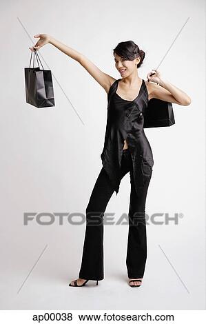 Young woman carrying shopping bags, standing with arm outstretched View Large Photo Image Stock Photo - Young woman carrying shopping bags, standing with arm outstretched. Fotosearch