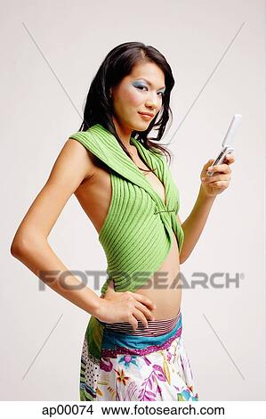 Young woman holding at mobile phone, hand on hip, looking at camera View Large Photo Image Picture - Young woman holding at mobile phone, hand on hip, looking at camera. Fotosearch