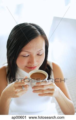 Stock Image - Young woman, holding cup of coffee, eyes closed. Fotosearch