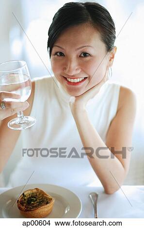 Picture - Young woman holding glass of water, smiling at camera. Fotosearch