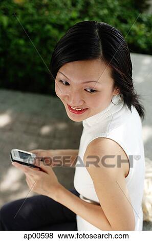Young woman, holding mobile phone, high angle view View Large Photo Image Stock Photo - Young woman, holding mobile phone, high angle view. Fotosearch