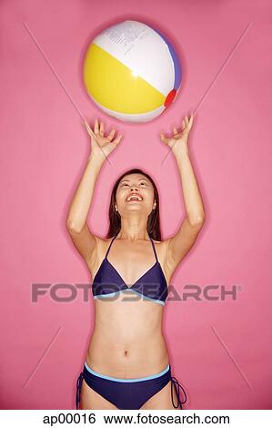 Stock Photograph - Young woman in bikini, tossing beach ball. Fotosearch