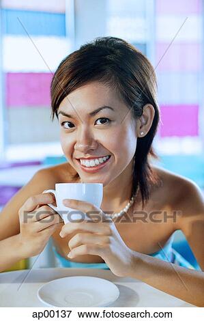 Stock Photo - Young woman looking at camera, holding cup and smiling. Fotosearch