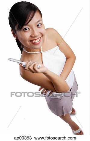 Stock Image - Young woman looking at camera, mobile phone in hand. Fotosearch