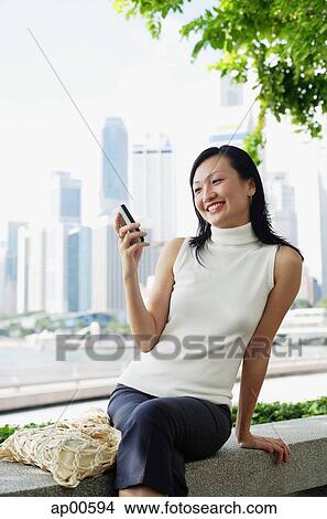 Picture - Young woman, looking at mobile phone, smiling. Fotosearch