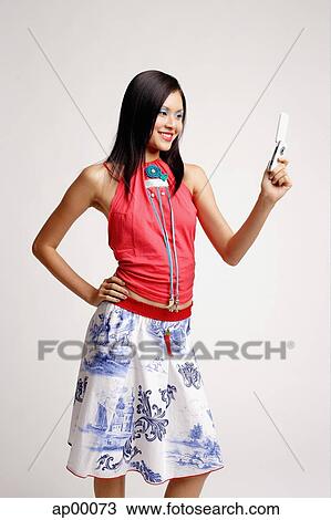 Stock Image - Young woman looking at mobile phone, hand on hip. Fotosearch