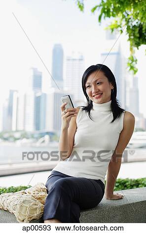 Young woman, looking at mobile phone, buildings in the background View Large Photo Image Stock Image - Young woman, looking at mobile phone, buildings in the background. Fotosearch