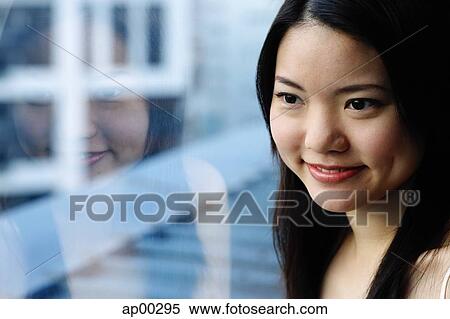 Stock Photography - Young woman looking through window, portrait. Fotosearch