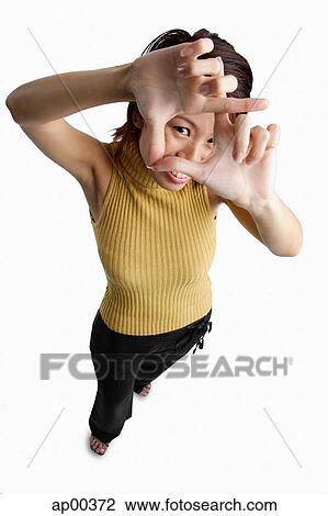Stock Image - Young woman looking up at camera, through her hands. Fotosearch