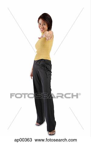 Stock Image - Young woman standing, hand pointing towards camera. Fotosearch
