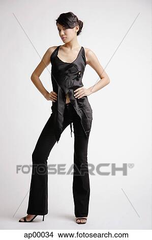 Picture - Young woman standing with hands on hips, looking at camera. Fotosearch