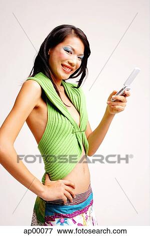 Stock Photo - Young woman with mobile phone, hand on hip, smiling at camera. Fotosearch