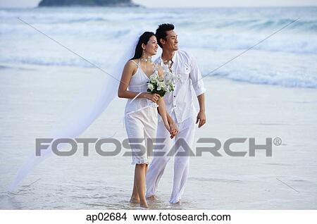 Bride and groom walking on beach, holding hands, looking away View Large Photo Image Picture - Bride and groom walking on beach, holding hands, looking away. Fotosearch