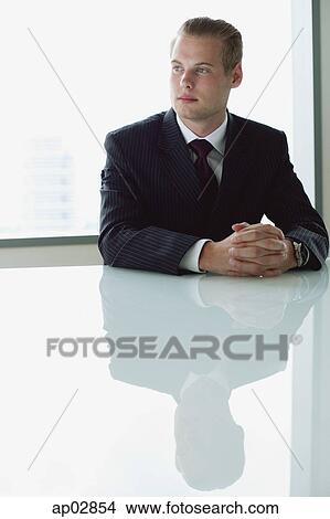 Businessman sitting at table, looking away View Large Photo Image Picture - Businessman sitting at table, looking away . Fotosearch