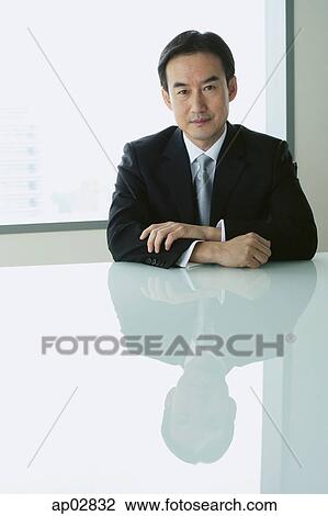 Businessman sitting at table, looking at camera View Large Photo Image Stock Image - Businessman sitting at table, looking at camera . Fotosearch