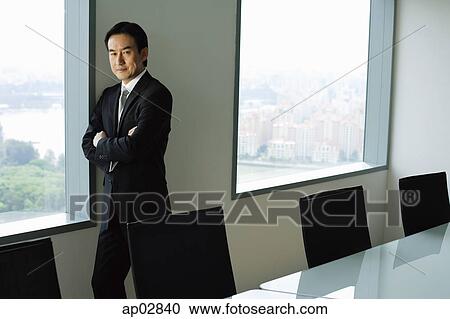 Stock Image - Businessman standing next to window in conference room, looking at camera . Fotosearch