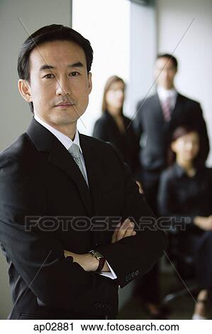 Businessman standing with arms crossed, people in the background View Large Photo Image Stock Image - Businessman standing with arms crossed, people in the background . Fotosearch