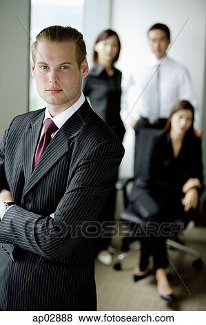 Businessman standing with arms crossed, people in the background View Large Photo Image Stock Photo - Businessman standing with arms crossed, people in the background . Fotosearch