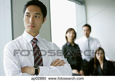 Businessman standing with arms crossed, looking away, people in the background View Large Photo Image Stock Photography - Businessman standing with arms crossed, looking away, people in the background . Fotosearch