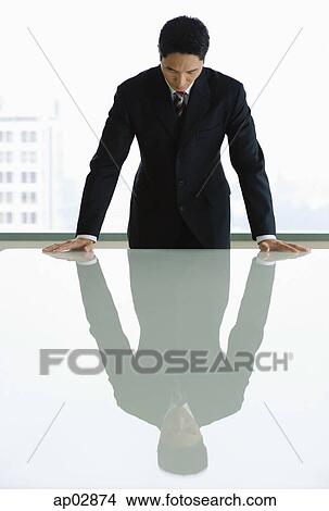 Picture - Businessman standing with hands on table, looking down . Fotosearch