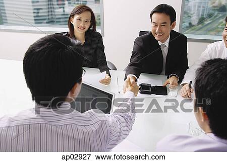 Businessmen in meeting, shaking hands across table View Large Photo Image Stock Photo - Businessmen in meeting, shaking hands across table. Fotosearch