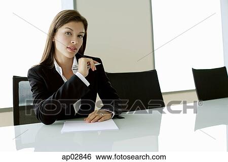 Businesswoman sitting at table, holding pen, looking at camera View Large Photo Image Stock Photograph - Businesswoman sitting at table, holding pen, looking at camera . Fotosearch