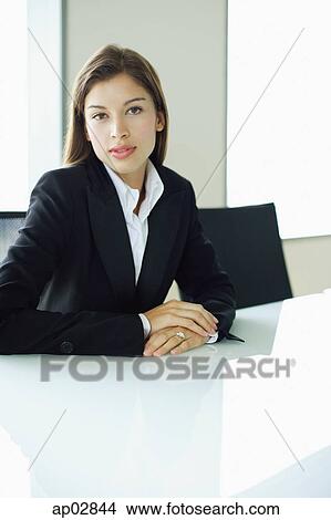 Businesswoman sitting at table, looking at camera View Large Photo Image Picture - Businesswoman sitting at table, looking at camera . Fotosearch