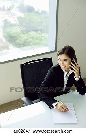 Stock Photo - Businesswoman sitting at table, using mobile phone, looking away . Fotosearch