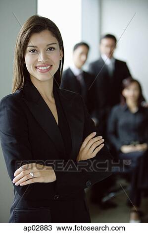 Businesswoman standing with arms crossed, smiling, people in the background View Large Photo Image Stock Image - Businesswoman standing with arms crossed, smiling, people in the background . Fotosearch