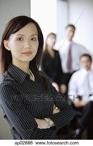 Businesswoman standing with arms crossed, looking at the camera, people in the background View Large Photo Image Stock Photograph - Businesswoman standing with arms crossed, looking at the camera, people in the background . Fotosearch