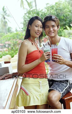 Couple at beach bar, holding drinks, looking at camera View Large Photo Image Stock Image - Couple at beach bar, holding drinks, looking at camera . Fotosearch