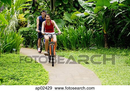 Stock Photo - Couple cycling leisurely through a park . Fotosearch