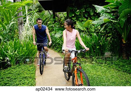 Couple cycling on a path through a park View Large Photo Image Picture - Couple cycling on a path through a park . Fotosearch