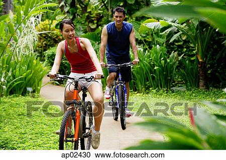 Couple cycling through a park, smiling View Large Photo Image Stock Image - Couple cycling through a park, smiling . Fotosearch