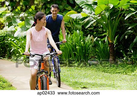Stock Image - Couple cycling together through a park . Fotosearch