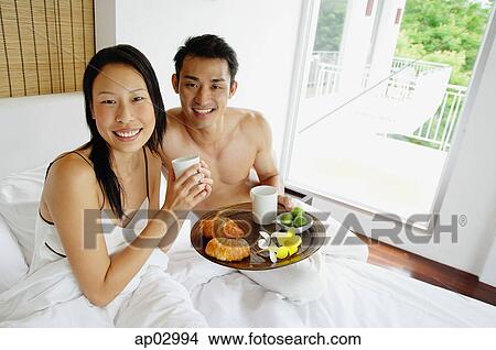 Couple having breakfast in bed, looking at camera View Large Photo Image Picture - Couple having breakfast in bed, looking at camera. Fotosearch