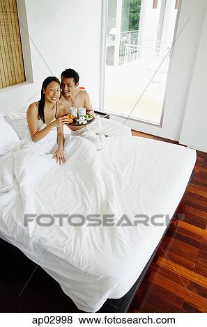 Couple having breakfast in bed, woman smiling at camera, high angle view View Large Photo Image Stock Photo - Couple having breakfast in bed, woman smiling at camera, high angle view . Fotosearch