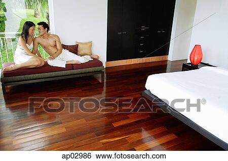 Stock Photograph - Couple in bedroom, sitting on daybed, looking at each other . Fotosearch