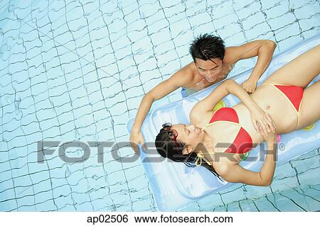 Couple in swimming pool, woman lying on pool raft, man next to her View Large Photo Image Stock Photograph - Couple in swimming pool, woman lying on pool raft, man next to her . Fotosearch