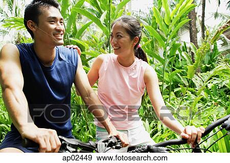 Stock Photo - Couple on bikes, woman with hand on mans shoulder. Fotosearch