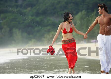 Couple running along beach, ankle deep in water, holding hands View Large Photo Image Stock Photo - Couple running along beach, ankle deep in water, holding hands . Fotosearch