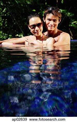 Stock Photo - Couple sitting in swimming pool, smiling at camera . Fotosearch