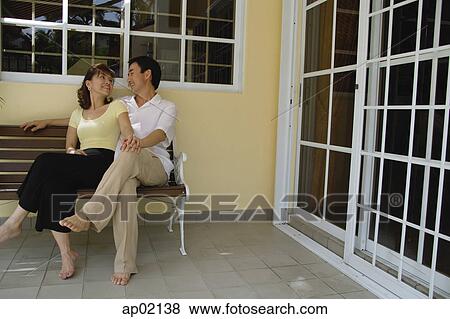 Stock Photo - Couple sitting on bench in patio, looking at each other . Fotosearch
