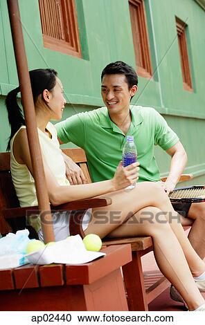 Couple sitting on bench on tennis court, smiling at each other, woman with legs crossed View Large Photo Image Stock Image - Couple sitting on bench on tennis court, smiling at each other, woman with legs crossed . Fotosearch