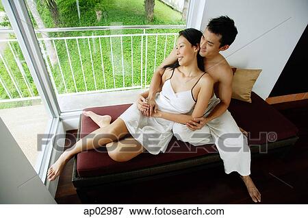 Stock Photo - Couple sitting on daybed next to window, embracing . Fotosearch