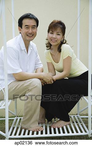 Couple sitting on swing, holding hands and looking at the camera View Large Photo Image Stock Photograph - Couple sitting on swing, holding hands and looking at the camera . Fotosearch