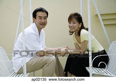 Couple sitting on swing, holding hands, looking at the camera View Large Photo Image Stock Photography - Couple sitting on swing, holding hands, looking at the camera . Fotosearch